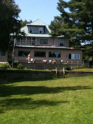 The Glenmore seen from the lawn on the lake side, people sitting out along the deck rail on a summer afternoon