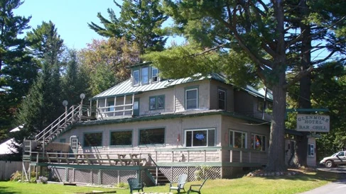 The Glenmore from Glenmore Road: a long shingled building with a green metal roof, a deck along the front, an outside staircase, tall pines behind it, and the Glenmore Bar and Grill sign on a post at the roadside